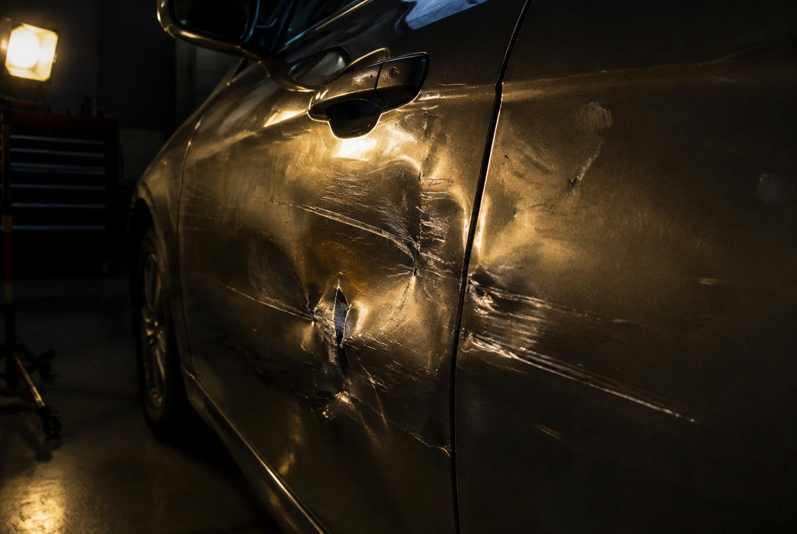 A car door panel with dents and scratches before repair, lit by a workshop lamp